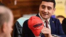 a man in a suit and tie is holding a trump hat