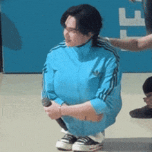 a person wearing a blue adidas jacket is squatting down holding a microphone .
