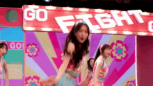 a group of girls are dancing in front of a sign that says " go fight "