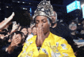 a man wearing a crown and a yellow jacket stands in front of a crowd of people