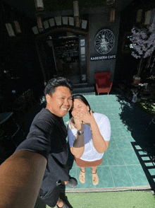 a man and woman pose for a photo in front of a kabesara cafe