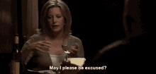 a woman sits at a table with a glass of wine and says may i please be excused ..