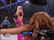 a woman in a pink bikini is standing in a wrestling ring with a w logo on her back
