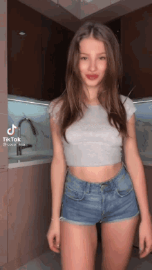 a girl in a crop top and shorts is standing in a kitchen .