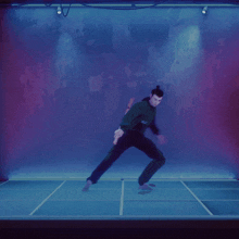 a man is dancing in a dark room with a purple wall behind him