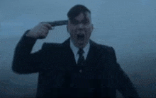 a man in a suit is holding a gun to his head .