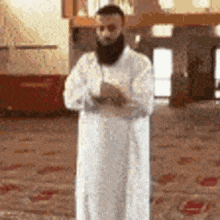 a man with a beard in a white robe is praying in a mosque .