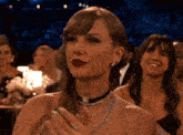 a woman wearing a choker and a necklace is clapping her hands in a crowd of people .