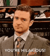 a man in a suit and tie is making a funny face and saying `` you 're hilarious ! ''
