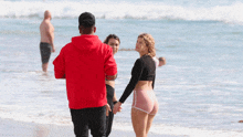 a man in a red hoodie stands next to two women on the beach