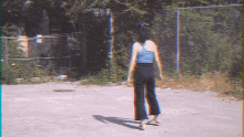 a woman in a blue tank top and black pants stands in a parking lot