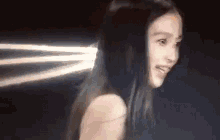 a close up of a woman 's face in a dark room with a light coming out of her hair .
