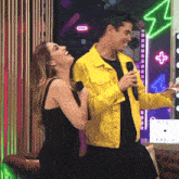 a man in a yellow jacket is holding a microphone while a woman laughs