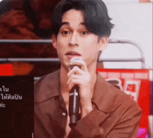 a man in a brown shirt is holding a microphone and making a face .