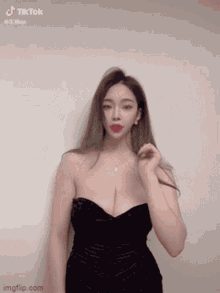 a woman in a black strapless dress is standing in front of a wall .