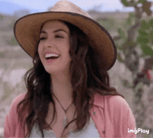a woman wearing a straw hat and a pink shirt laughs