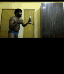 a shirtless man in blue underwear is holding a bottle of champagne