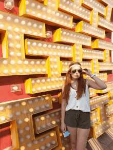 a woman wearing sunglasses and a headband stands in front of a maze of lights