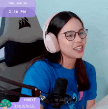 a woman wearing headphones and a blue shirt is sitting in front of a microphone with a purple box that says forest