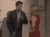 a man in a leather jacket and a woman in a red dress are standing next to each other in a hallway .