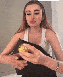 a woman in a white tank top is holding a gold object