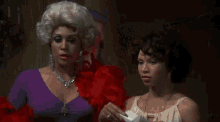 two women are standing next to each other in a room . one of the women is holding a piece of paper .
