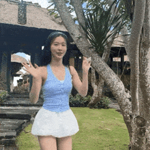 a woman in a blue tank top and white skirt is standing in front of a tree