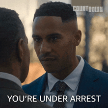 a man in a suit and tie talks to another man with the words " you 're under arrest " written below him