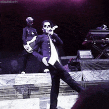 a man in a suit is singing into a microphone while another man plays a guitar in the background
