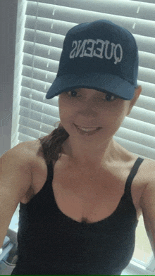 a woman wearing a black tank top and a blue hat that says queenz