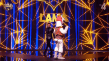 a man in a black suit is standing next to a llama mascot on a stage