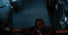 a man is standing in a dark room with his arms outstretched and looking down .