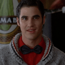 a man wearing a red shirt and a bow tie stands in front of a sign that says ima b.