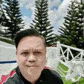 a man taking a selfie in front of a white fence and trees