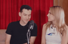 a man and a woman are looking at each other in front of a microphone in a room .