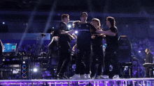 a group of people are standing on a stage with their arms outstretched and one of their shirts has the letter g on it