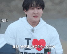 a young man wearing a white hoodie with a red heart and the letter i on it .