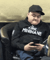 a man wearing a hoodie that says kirk minihane looks at his phone