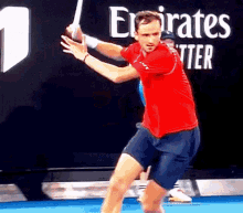a man in a red shirt is swinging a tennis racket on a blue court .