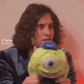 a man with long hair is holding a stuffed mike from monsters inc.