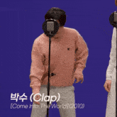 a man in a pink sweater and white pants is standing in front of a microphone with the word clap on it