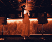 a woman in a red dress stands in front of a bar in a dark room