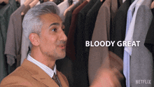 a man in a suit and tie is standing in front of a rack of clothes and the words bloody great are above him