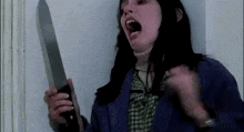 a woman in a blue jacket is holding a large knife in her hand .