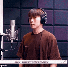 a young man wearing headphones and a brown shirt stands in front of a microphone ..