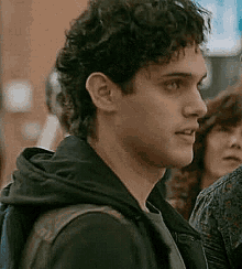 a man with curly hair is wearing a black hoodie and a backpack .