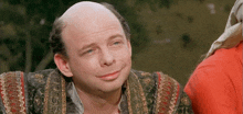a man with a bald head and a red shirt is smiling for the camera