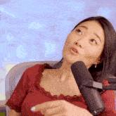 a woman in a red top is sitting in front of a microphone and pointing