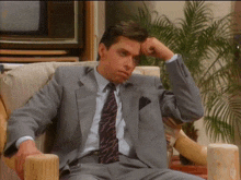 a man in a suit sits in a chair with his hand on his head