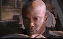 a bald man is sitting in the driver 's seat of a car and looking at the camera .